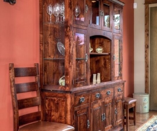 Six door china cabinet with glass doors on top and four wooden doors against a red wall with a matching chair next to it